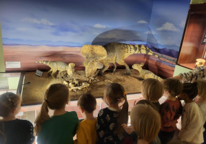 Zdjęcie przedstawia dzieci oglądające eksponaty dinozaurów.