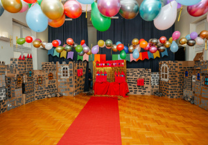 Sala udekorowana kolorowymi balonami oraz konstrukcjami z kartonów przypominający zabudowania zamku. Przez środek sali prowadzi czerwony dywan do tronu króla i królowej.