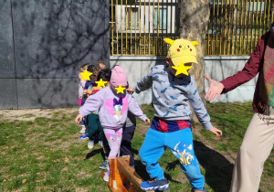 Zdjęcie przedstawia chłopca próbującego złapać równowagę stojąc na ławce gimnastycznej. W tle widać obserwujące chłopca dzieci.