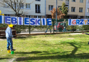 Na zdjęciu widać napis NIEBIESKIE IGRZYSKA oraz dziewczynkę i chłopca poruszających się na szczudłach gimnastycznych