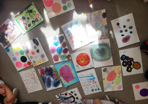 Zdjęcie przedstawia prace plastyczne z kolorowymi kropkami, na środku leży książki "Kropka"