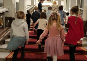 Zdjęcie przedstawia grupę dzieci wchodzących po schodach po czerwonym dywanie.