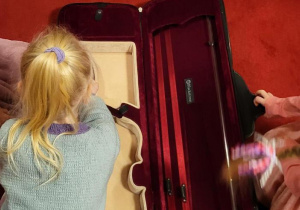 Zdjęcie przedstawia dziewczynkę pochylającą się nad futerałem na skrzypce.