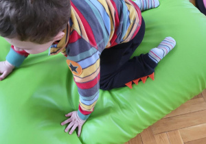 Chłopiec w bluzie w kolorowe paski siedzi na dużej zielonej poduszce sensorycznej