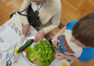 Dziecko z babcią przy talerzu z warzywami: ogórkiem zielonym, sałatą