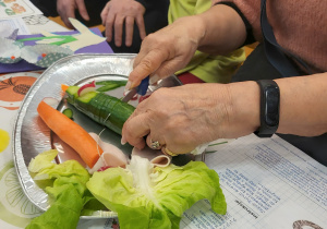 Ręce starszej osoby krojącej zielonego ogórka leżącego na srebrny talerzu