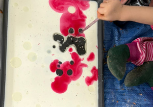 ręce wyciskające pipętą kolorowy barwnik na tace z białym płynem