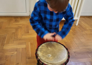 Chłopiec w kosuli w czarno niebieską kratę stojący przy bębnie afrykańskim