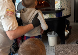Mężczyzna podnosi chłopca tak aby ten zobaczył duży kamienny piec do wypiekania pizzy